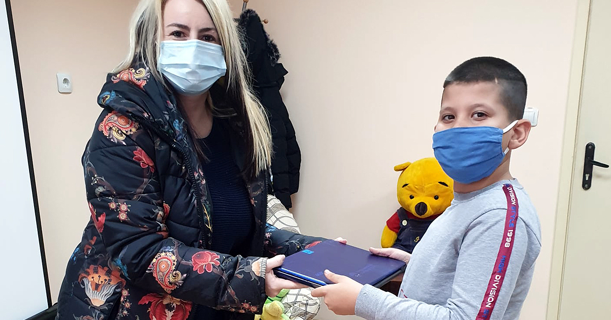 A chiled receives a laptop from a member of the Anglof Regional Foundation & Humanitarian Relief Agency (ARFHRA) Bulgaria team
