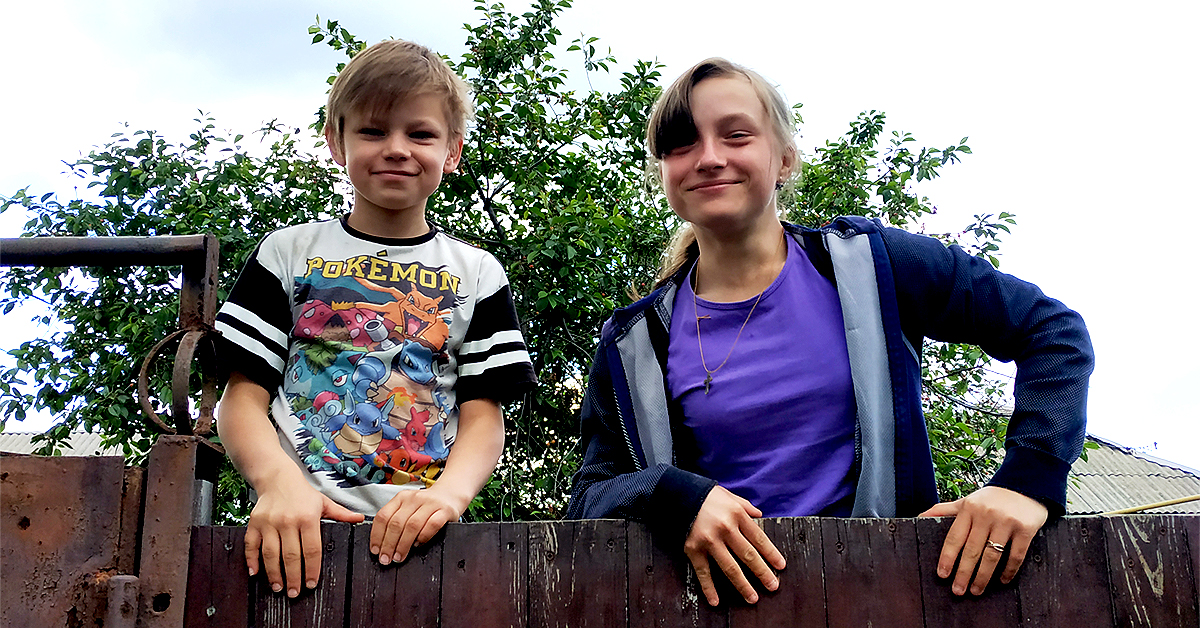 Maksym and Anya, brother and sister, climbing over a gate, smiling 